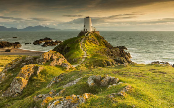 A 4K Ultra HD wallpaper of a lighthouse on a grassy coastal path overlooking the ocean and horizon under a dramatic sky.