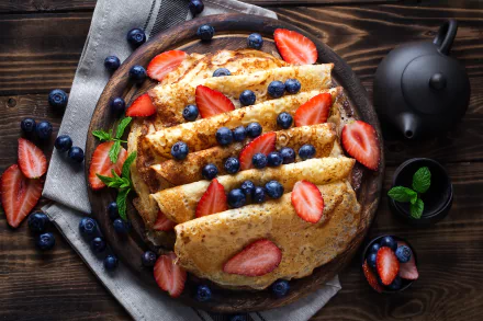 A close-up of crepes topped with fresh strawberries and blueberries, presented on a rustic plate with a dark wooden background, captured in 4K Ultra HD.