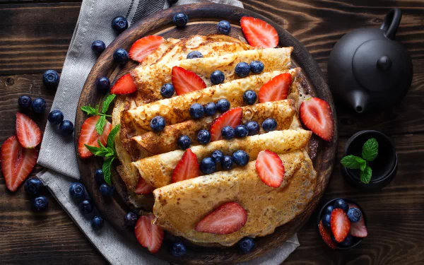 A close-up of crepes topped with fresh strawberries and blueberries, presented on a rustic plate with a dark wooden background, captured in 4K Ultra HD.