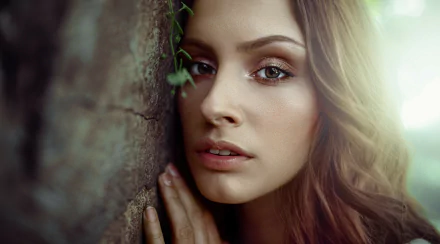 HD PC desktop wallpaper and background showing a brunette model woman's face in close-up, soft lighting, hand against a textured wall, warm detailed portrait.