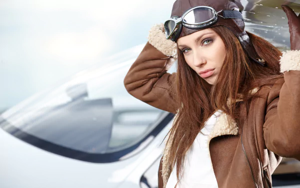 Redhead woman model with blue eyes wearing an aviator helmet and brown shearling jacket, posed in front of a small aircraft, captured in 4K Ultra HD quality.