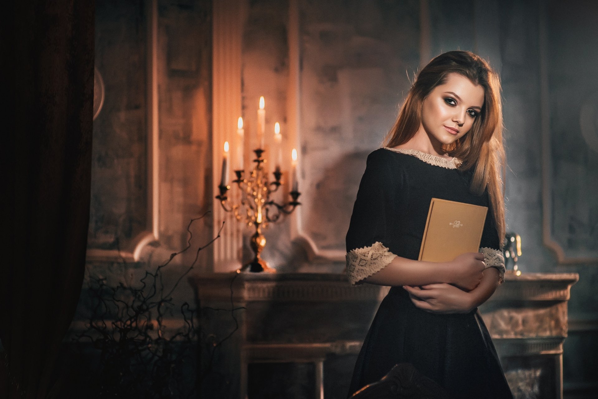 HD PC desktop wallpaper of a brunette model in a black dress holding a book in a candlelit vintage room.