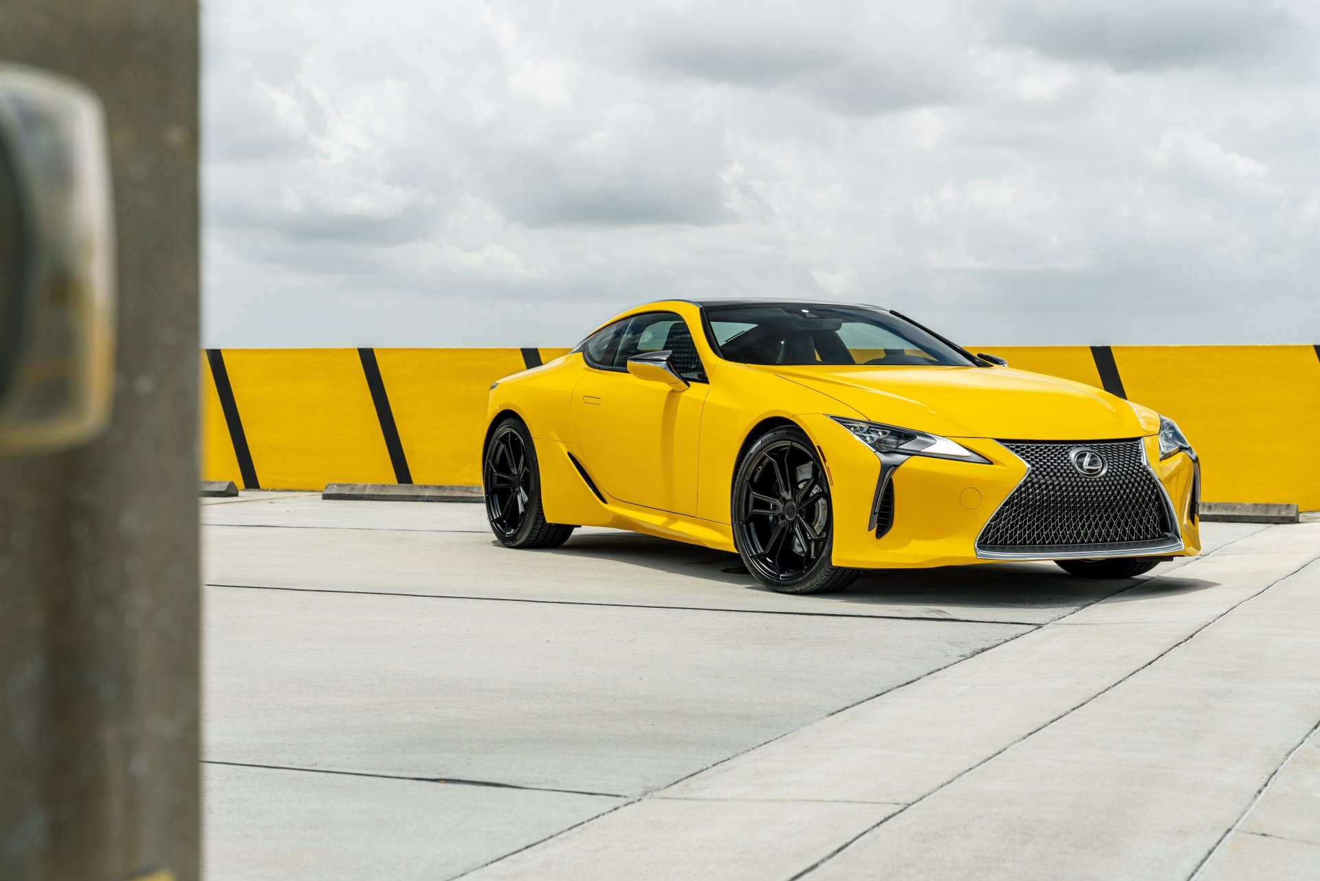 Yellow Lexus LC 500 supercar parked on a rooftop against a yellow-striped barrier and cloudy sky, presented as an 8K Ultra HD PC desktop wallpaper/background.