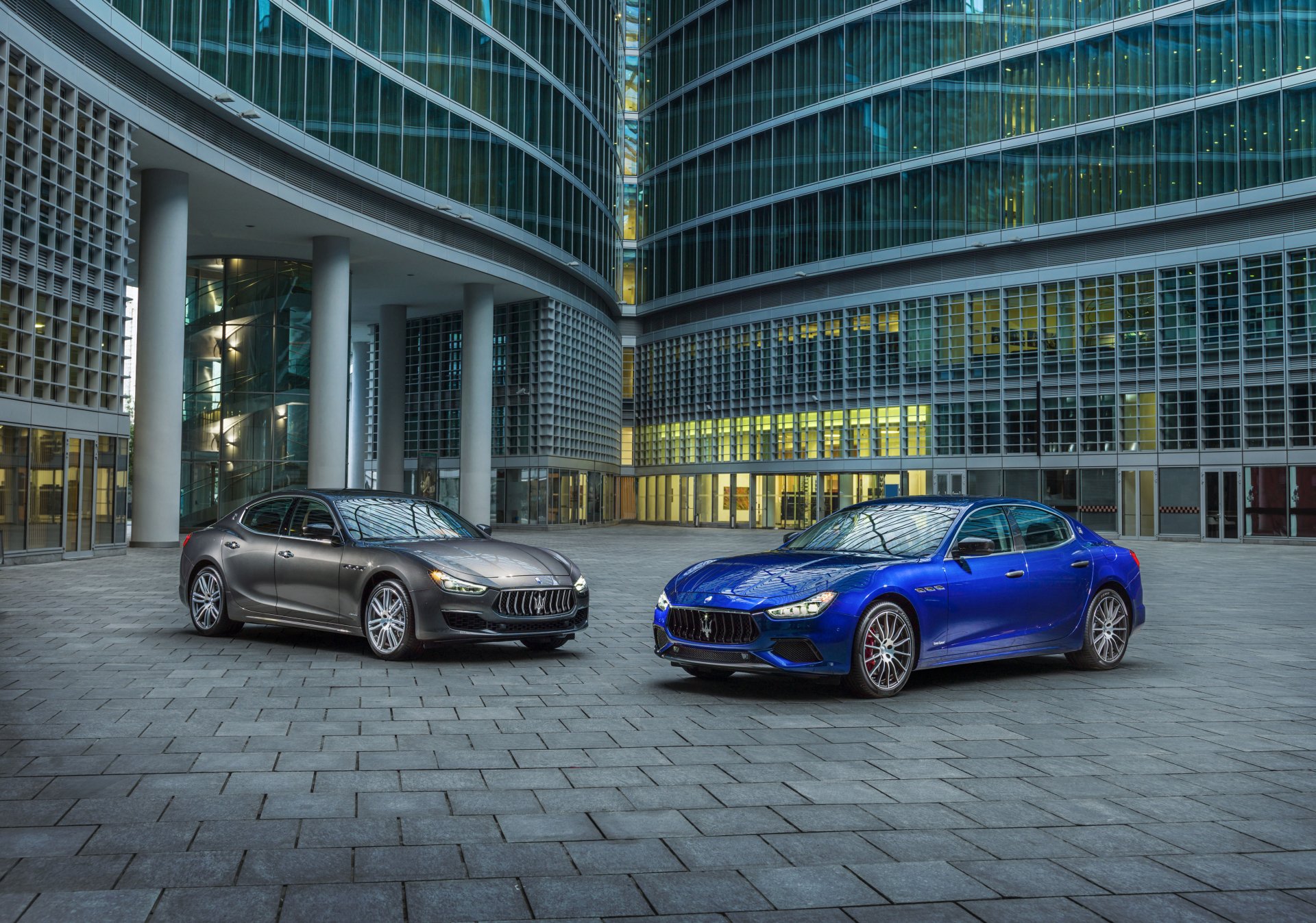 Silver and blue Maserati Ghibli sedans parked before a curved glass office tower, 4K Ultra HD PC desktop wallpaper background.
