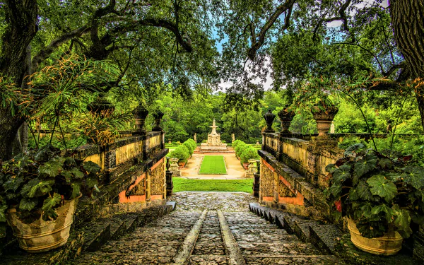 A lush green park in Florida featuring a cobblestone pathway framed by large trees and historic stone railings, captured in vibrant 4K Ultra HD detail.