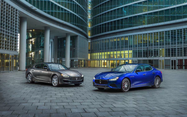 Silver and blue Maserati Ghibli sedans parked before a curved glass office tower, 4K Ultra HD PC desktop wallpaper background.