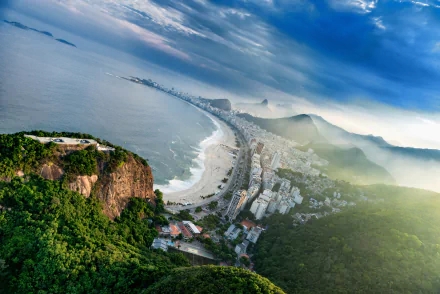 Aerial 5K Ultra HD desktop wallpaper of Copacabana beach in Rio de Janeiro, showing the man-made beachfront promenade curving along the coast with city skyline and misty hills.