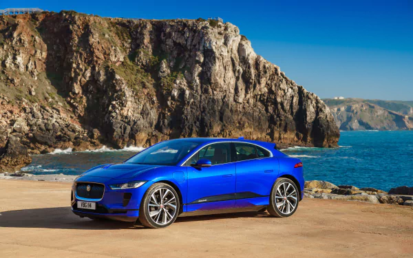 Blue Jaguar I-Pace vehicle parked on a coastal road with rocky cliffs and ocean in the background, captured in vibrant 4K Ultra HD detail.