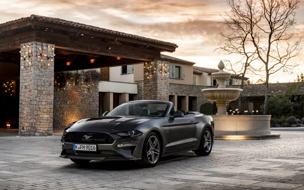 Black Ford Mustang GT cabriolet muscle car parked in front of a stone building with a fountain, captured in 4K Ultra HD for PC desktop wallpaper.