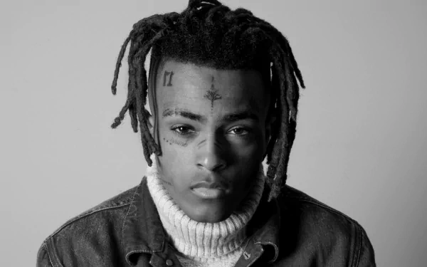 Black and white HD desktop wallpaper of XXXTentacion, featuring the artist with a neutral expression, wearing a denim jacket and a turtleneck sweater, against a plain background.
