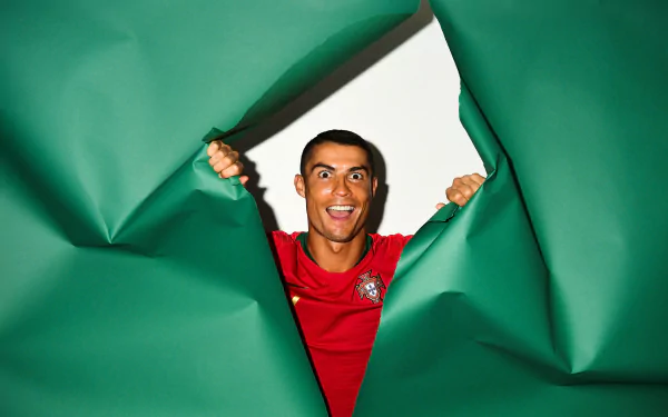 Cristiano Ronaldo in a red Portuguese soccer jersey bursts through a torn green backdrop, captured in vibrant 4K Ultra HD for a dynamic sports wallpaper.