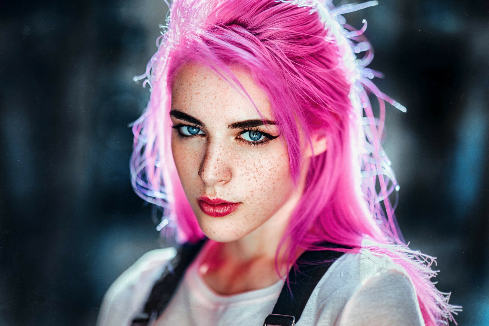 HD desktop wallpaper of a woman with vibrant pink hair, striking blue eyes, freckles, and bold lipstick, showcasing a captivating close-up portrait.