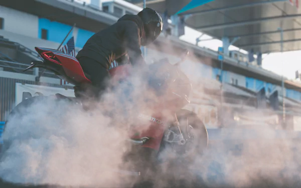 A 4K Ultra HD PC desktop wallpaper from The Crew 2 video game featuring a motorcyclist performing a burnout, creating smoke on a racetrack.