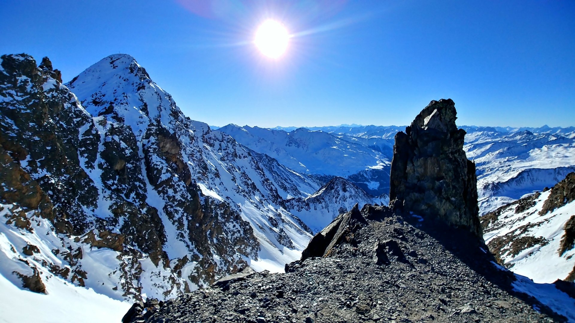 Snow-covered alpine landscape in Tyrol, featuring rugged mountains under a clear winter sky with bright sunlight, captured in HD for a desktop wallpaper background.