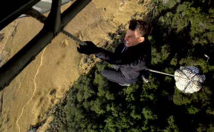 Stunt shot from Mission: Impossible – Fallout: a suited man dangles on a rope above cliffs and forest; 2K Quad HD PC desktop wallpaper/background.