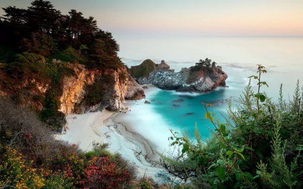 HD desktop wallpaper of a stunning coastal scene with a cliff, calm ocean, and a serene beach framed by lush greenery, showcasing the beauty of nature.