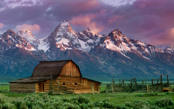 4K Ultra HD desktop wallpaper of a rustic barn in a green field with snow-capped mountains and dramatic cloud-filled sky in the background.