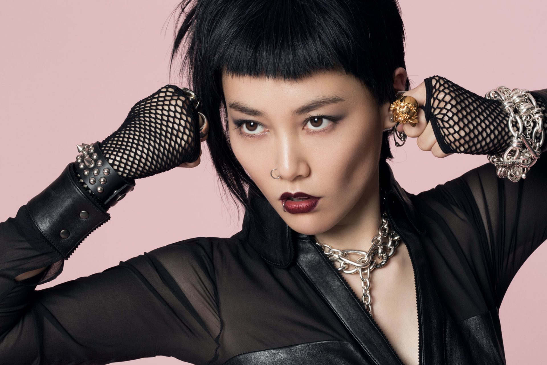 HD desktop wallpaper featuring a stylish individual with a bold makeup look, adorned with edgy jewelry against a pink background.