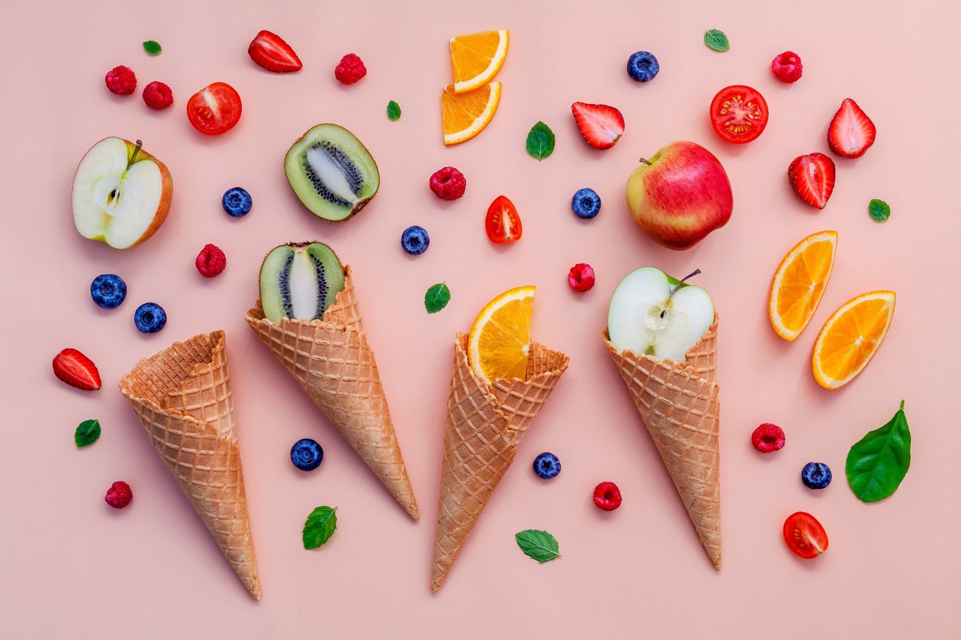 4K Ultra HD still life of fresh orange slices, apple halves, kiwi pieces, and berries artfully arranged with waffle cones on a soft pink background.