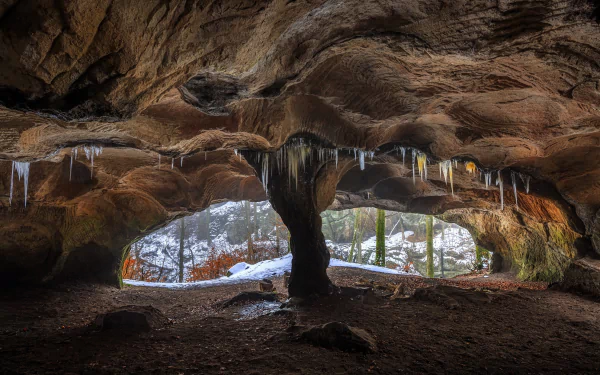 HD PC desktop wallpaper showcasing a nature scene of a cave interior with icicles hanging from the ceiling and a snowy landscape visible outside.