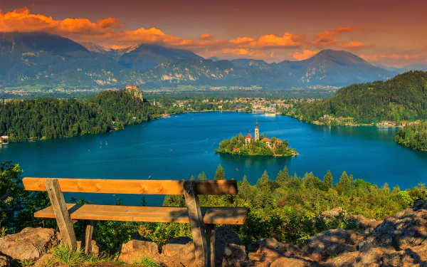 A vibrant 4K Ultra HD view of Lake Bled with its island and the Assumption of Mary Church, framed by mountains under a dramatic sunset sky.