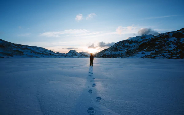 HD desktop wallpaper featuring a lone person standing on a vast snow-covered landscape with footprints leading back, framed by distant mountains under a clear sky.