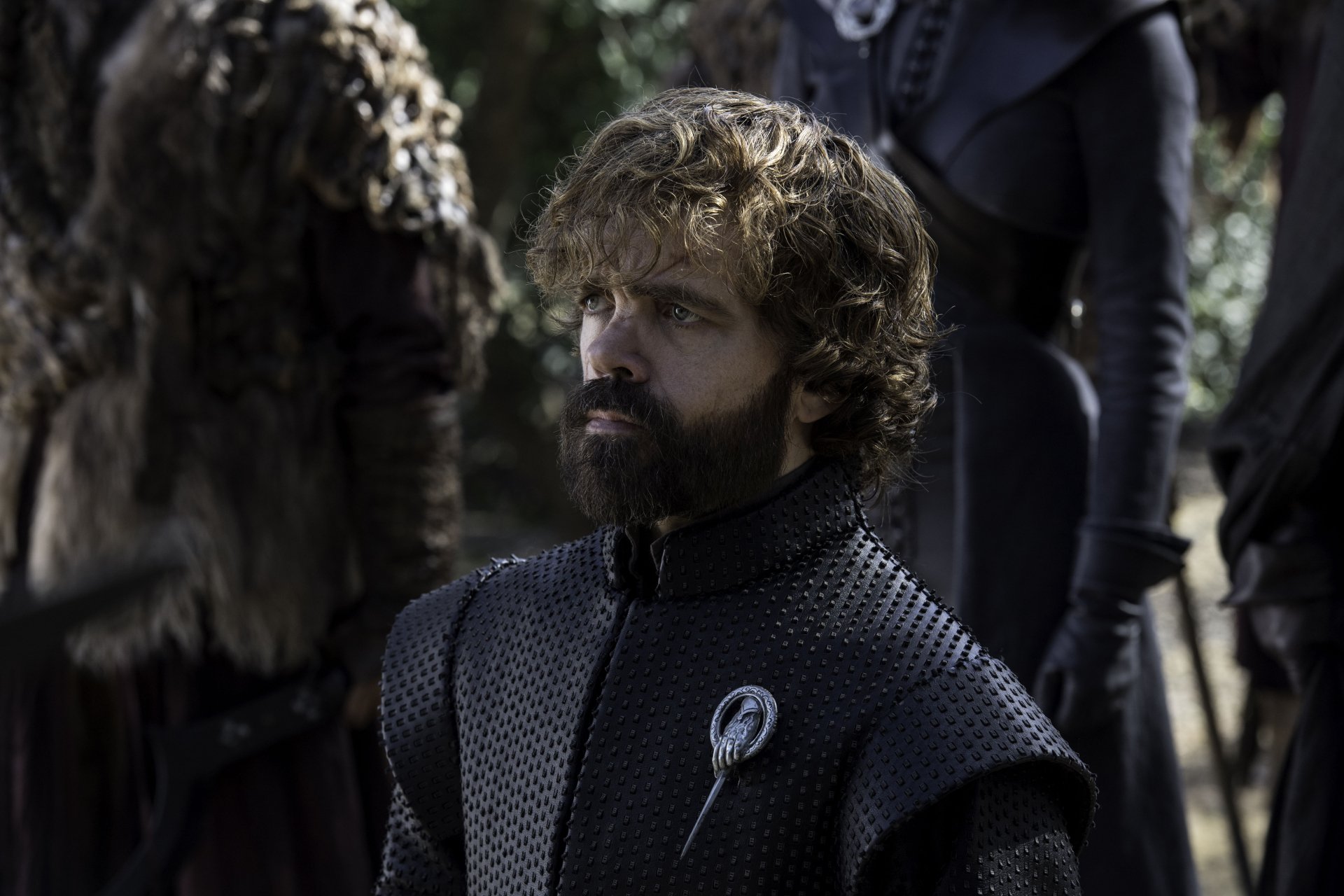 Tyrion Lannister (Game of Thrones) — bearded man in dark padded armor with a Hand brooch, gazing sideways amid cloaked figures; 5K Ultra HD TV-show PC desktop wallpaper.