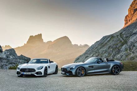 HD desktop wallpaper featuring a white and a silver Mercedes-AMG GT against a stunning mountainous backdrop at sunset.