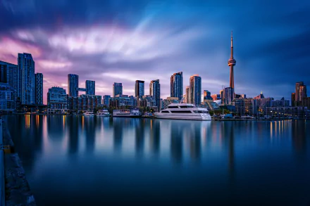 Toronto harbor at dusk with skyscrapers and the CN Tower reflecting on calm water, set against a vibrant sky. HD desktop wallpaper and background.
