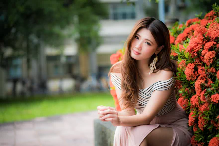 Asian brunette woman and model with long hair and brown eyes wearing dangling earrings, seated by red flowers; shallow depth of field, high-resolution 4K desktop wallpaper.