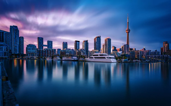 Toronto harbor at dusk with skyscrapers and the CN Tower reflecting on calm water, set against a vibrant sky. HD desktop wallpaper and background.