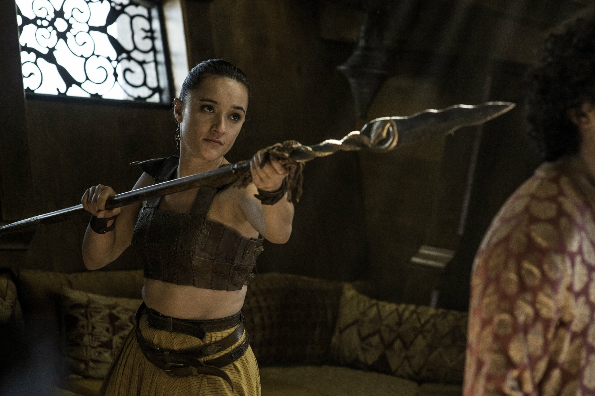 Game of Thrones TV show 4K Ultra HD PC desktop wallpaper/background: dim medieval room, a woman in leather armor grips a twisted spear, aiming tensely at an off-screen figure.