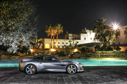 HD desktop wallpaper featuring a silver Ferrari Portofino supercar parked by a poolside at night with illuminated palm trees and a Mediterranean-style villa in the background.