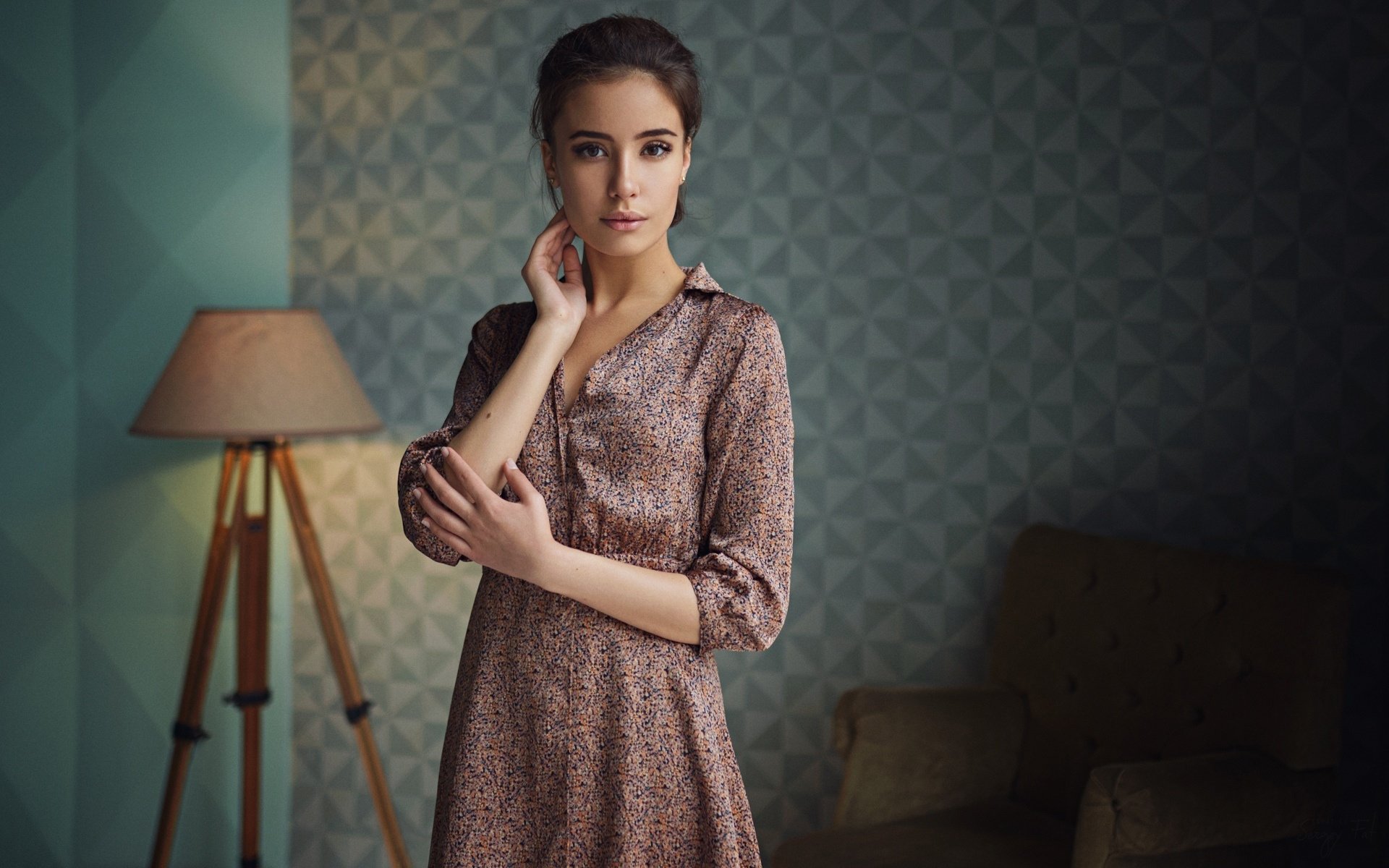 HD PC desktop wallpaper of a brunette model with brown eyes in a patterned dress, posing by a floor lamp in a softly lit room.