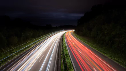 Time-lapse photography captures vibrant light trails of traffic on a winding road at night, presented in stunning 4K Ultra HD for a PC desktop wallpaper.