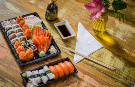HD desktop wallpaper featuring assorted sushi and seafood with chopsticks, soy sauce, and a flower vase on a wooden table in a vibrant still life composition.