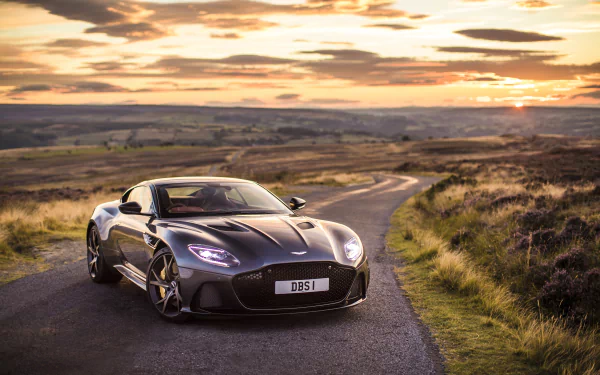 A sleek black Aston Martin DBS Superleggera supercar on a winding rural road at sunset, captured in 4K Ultra HD as a striking desktop wallpaper.