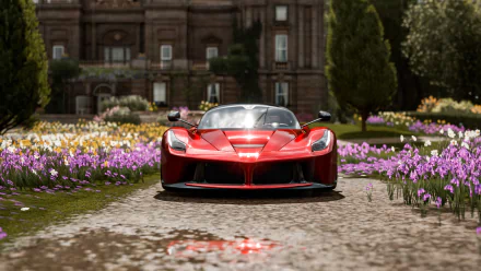 A red Ferrari LaFerrari showcased in 4K Ultra HD on a PC desktop wallpaper from the video game Forza Horizon 4, set on a flower-lined path with a historic building backdrop.