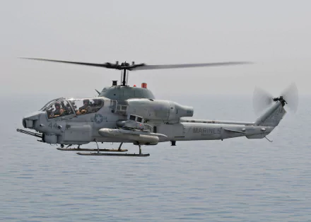 Bell AH-1 SuperCobra attack helicopter (military) hovering low over calm sea — HD PC desktop wallpaper.