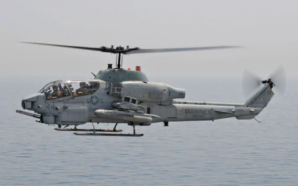 Bell AH-1 SuperCobra attack helicopter (military) hovering low over calm sea — HD PC desktop wallpaper.