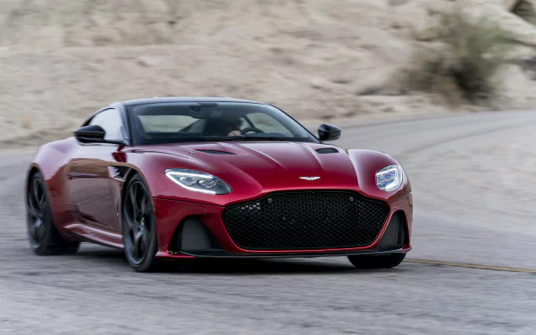 A red Aston Martin DBS Superleggera supercar driving on a winding road, captured in sharp detail for an HD PC desktop wallpaper.