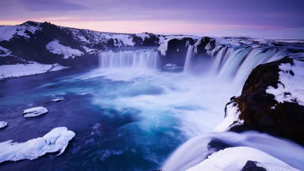 A breathtaking 8K Ultra HD image of Goðafoss waterfall surrounded by snow-covered rocks under a serene purple sky.