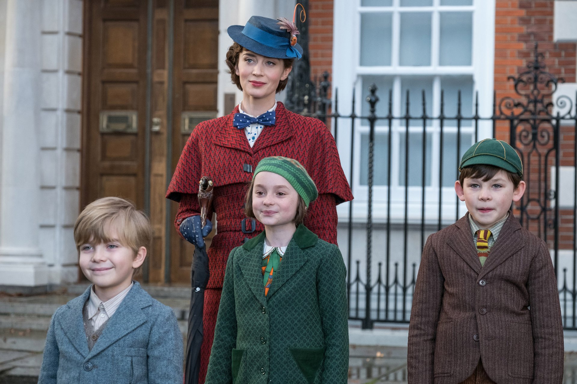 HD wallpaper featuring characters from Mary Poppins Returns, with Mary Poppins and three children in vintage attire standing in front of a house.