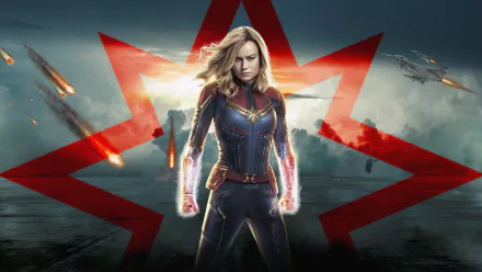 HD wallpaper featuring Brie Larson as Captain Marvel, posed heroically with a glowing energy effect, set against a dramatic sky and red star backdrop.