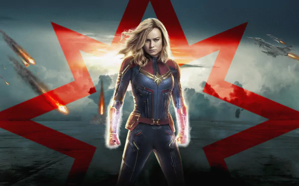 HD wallpaper featuring Brie Larson as Captain Marvel, posed heroically with a glowing energy effect, set against a dramatic sky and red star backdrop.