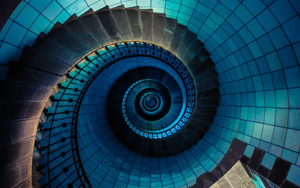 A 4K Ultra HD desktop wallpaper featuring a man-made spiral staircase viewed from above, showcasing its geometric curves and tiled walls in deep blue tones.