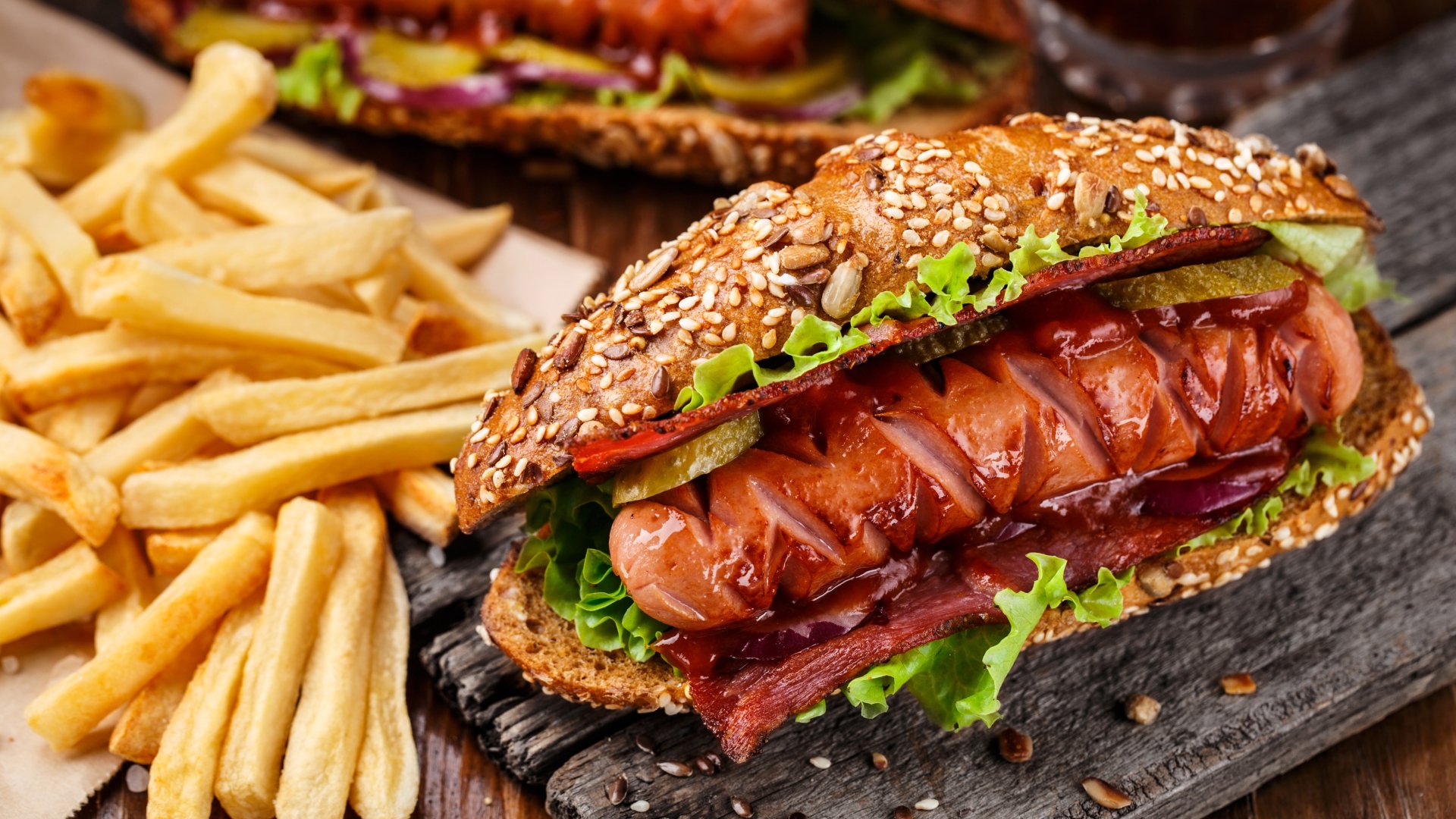 Close-up of a juicy hot dog with lettuce and bacon in a seeded bun, served with golden french fries, captured in stunning 4K Ultra HD detail.