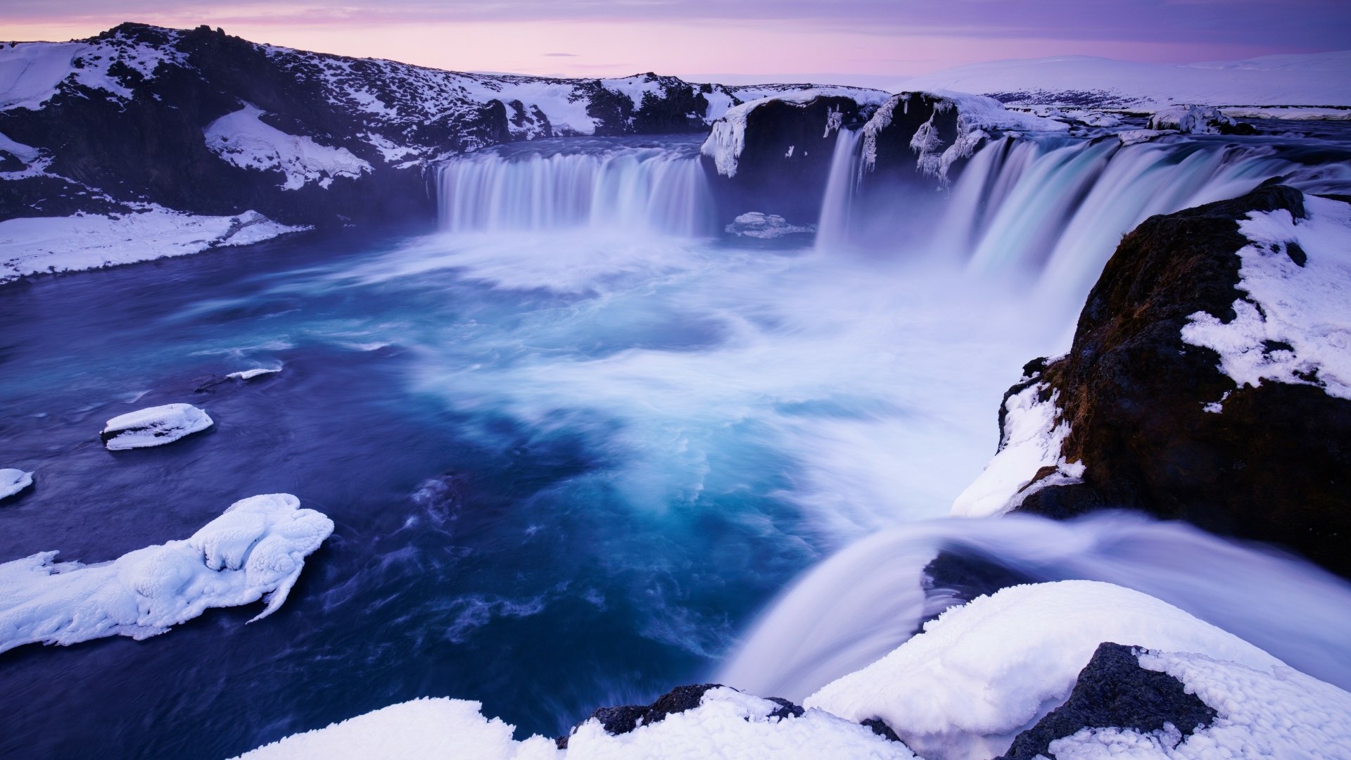 A stunning 4K Ultra HD winter nature scene featuring a majestic waterfall surrounded by snow-covered rocks and icy water, captured in vivid detail.