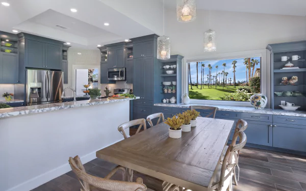 A bright, modern kitchen with blue cabinetry, wooden dining table, and large window showcasing a scenic outdoor view, captured in 4K Ultra HD for PC desktop wallpaper.
