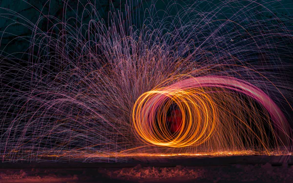 HD photography of fire juggling with vibrant trails of sparks swirling against a dark background, creating a dynamic and visually striking desktop wallpaper.